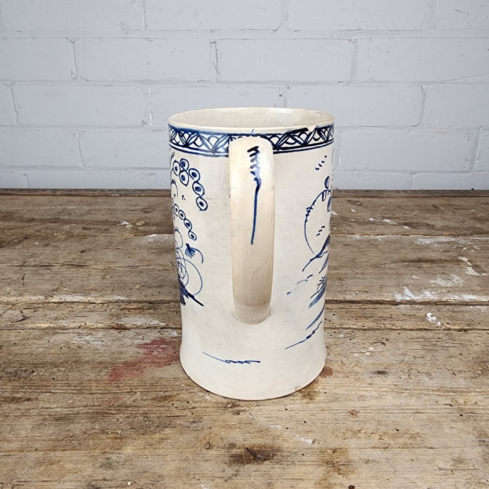 An antique cylindrical ceramic mug featuring blue and white hand-painted chinoiserie landscape decoration and an applied handle. View VIII
