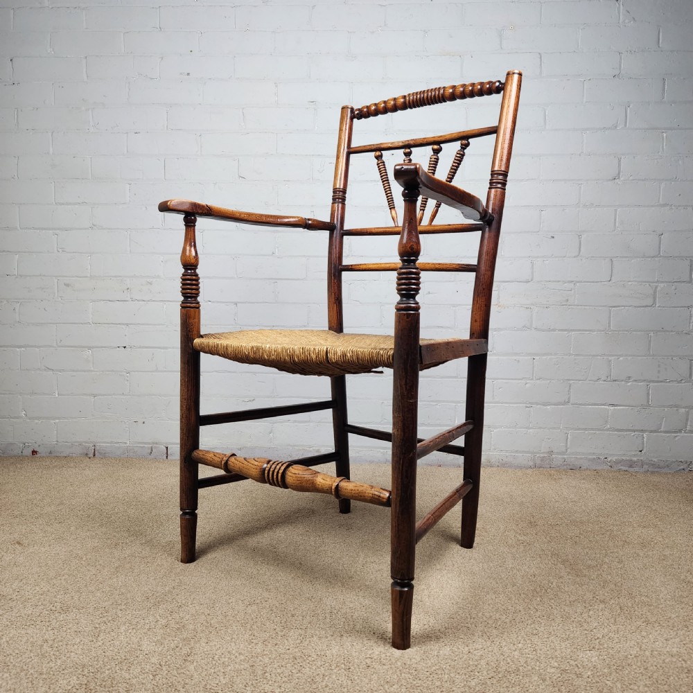 A George III elm and fruitwood carver chair featuring turned back spindles, shaped armrests, and a woven rush seat. View XIV