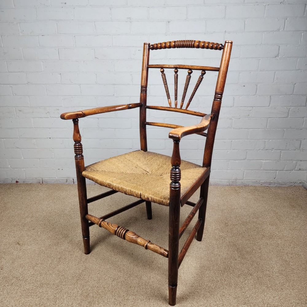 A George III elm and fruitwood carver chair featuring turned back spindles, shaped armrests, and a woven rush seat. View II
