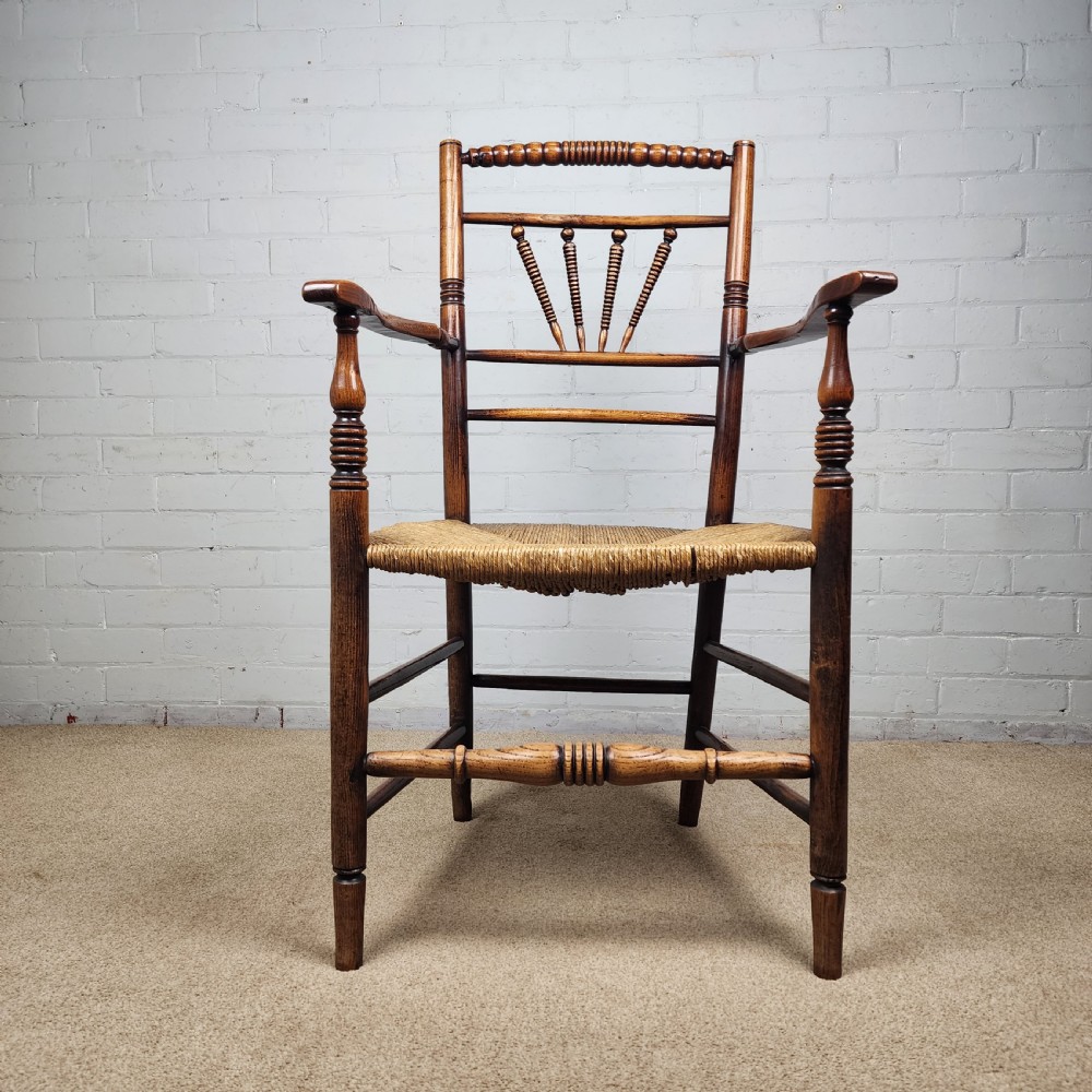 A George III elm and fruitwood carver chair featuring turned back spindles, shaped armrests, and a woven rush seat. View III