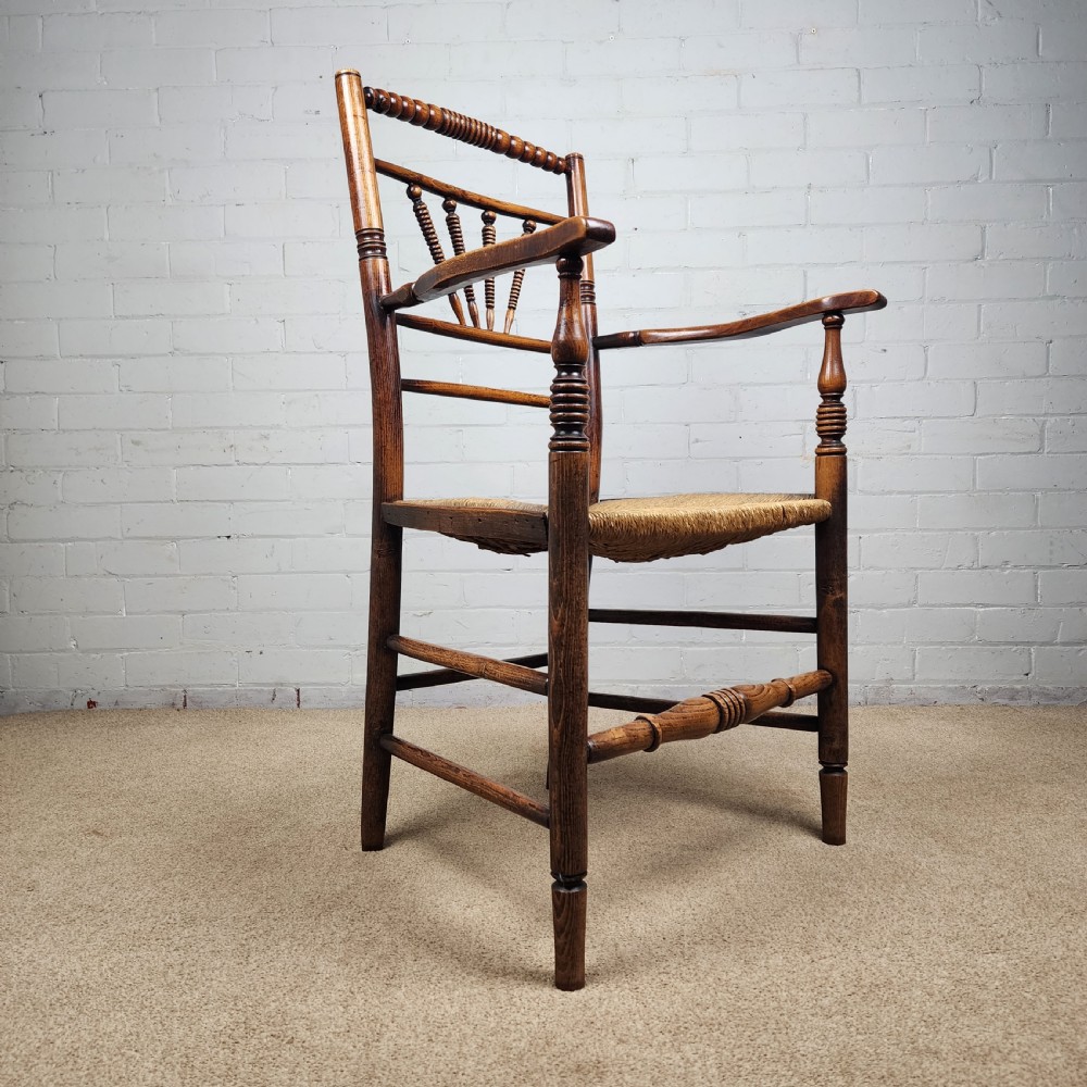 A George III elm and fruitwood carver chair featuring turned back spindles, shaped armrests, and a woven rush seat. View V