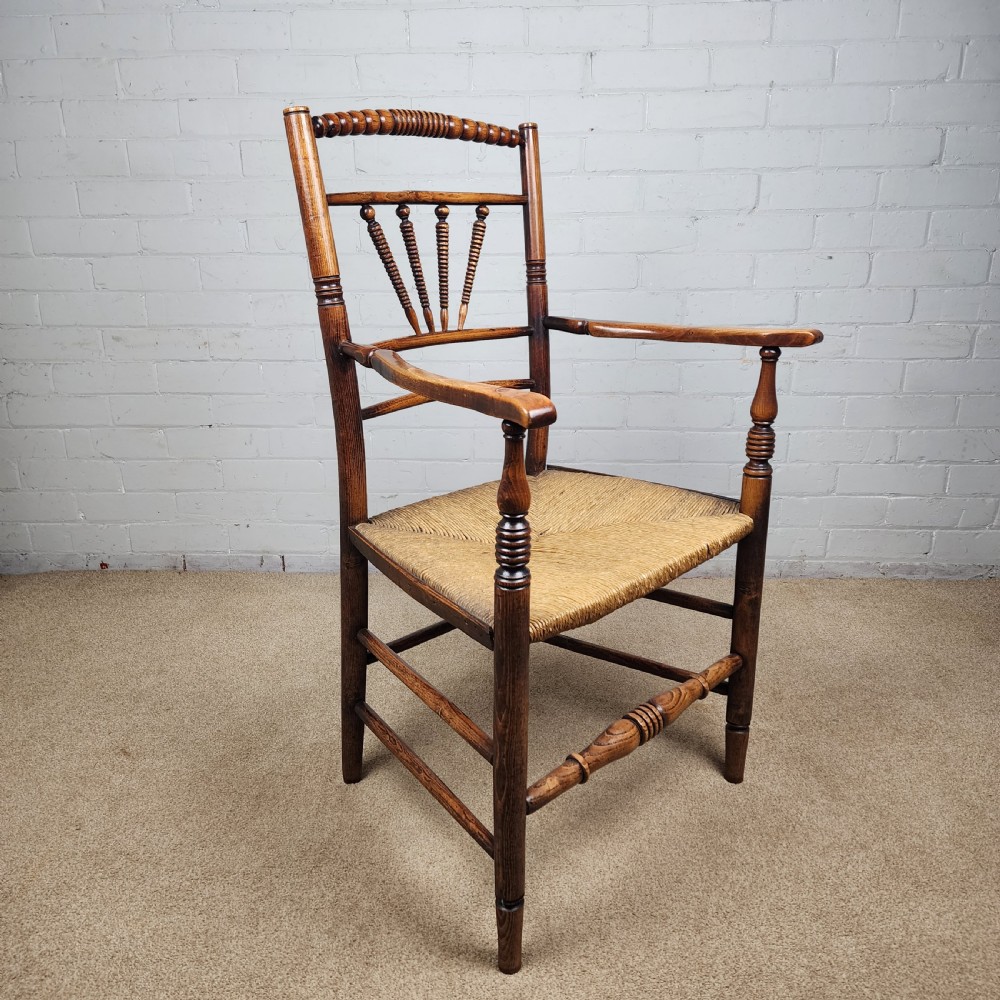 A George III elm and fruitwood carver chair featuring turned back spindles, shaped armrests, and a woven rush seat. View VI