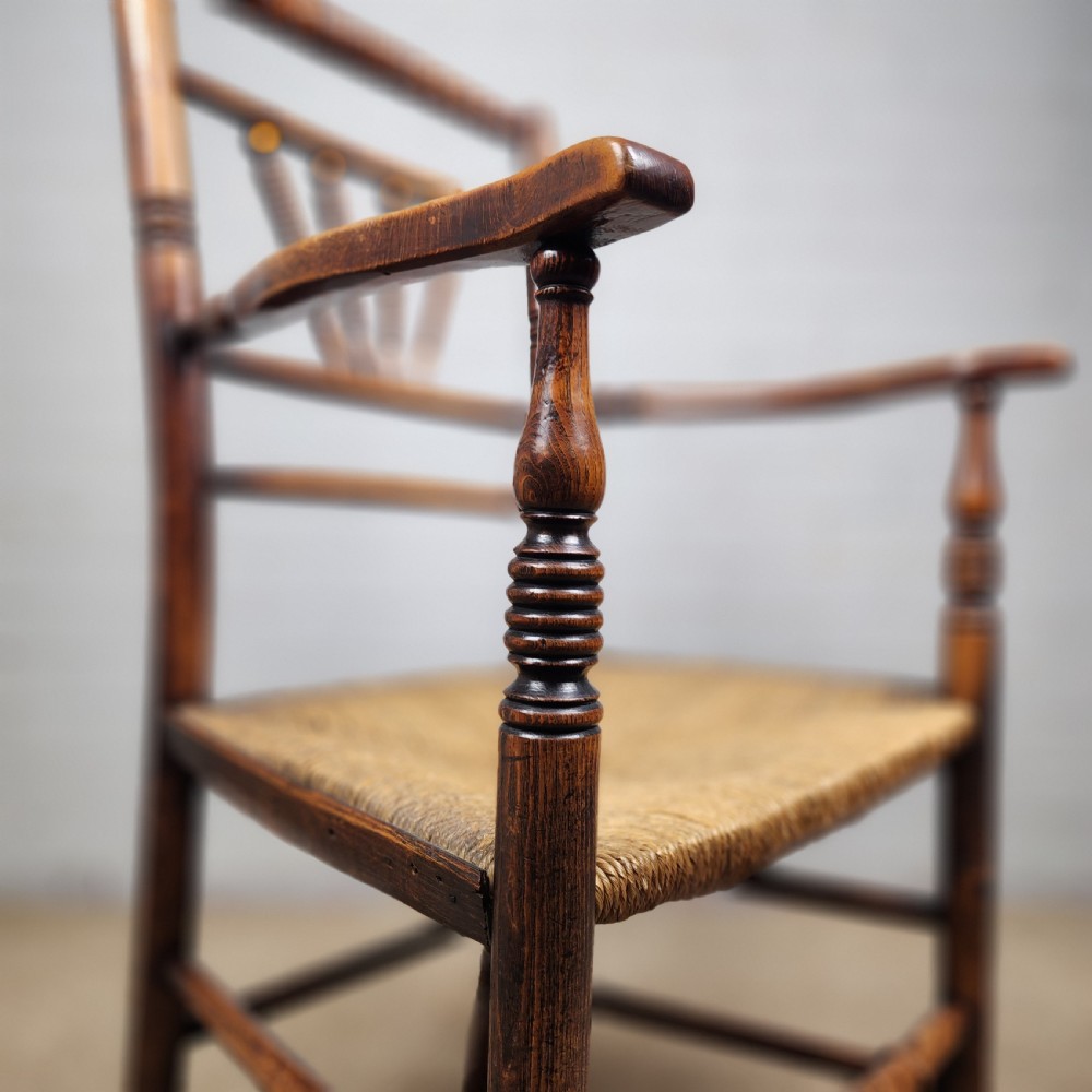 A George III elm and fruitwood carver chair featuring turned back spindles, shaped armrests, and a woven rush seat. View VII