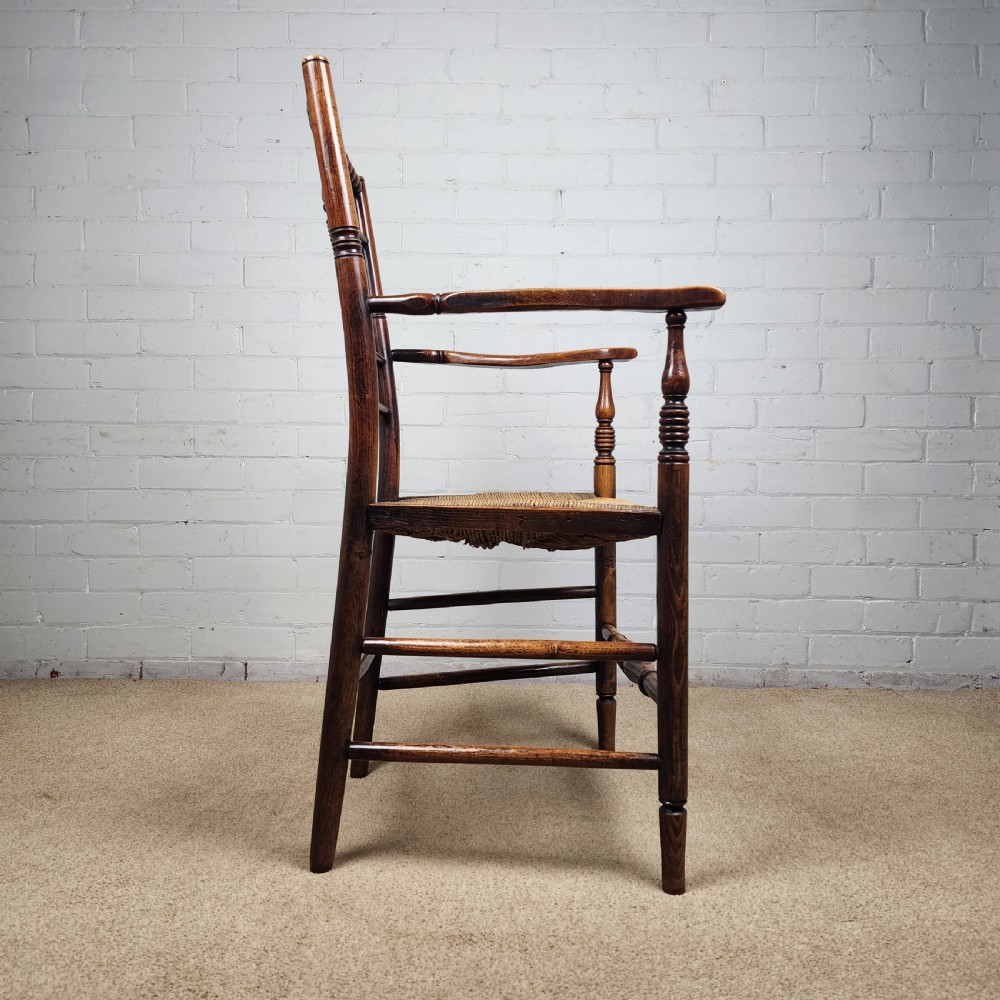 A George III elm and fruitwood carver chair featuring turned back spindles, shaped armrests, and a woven rush seat. View VIII