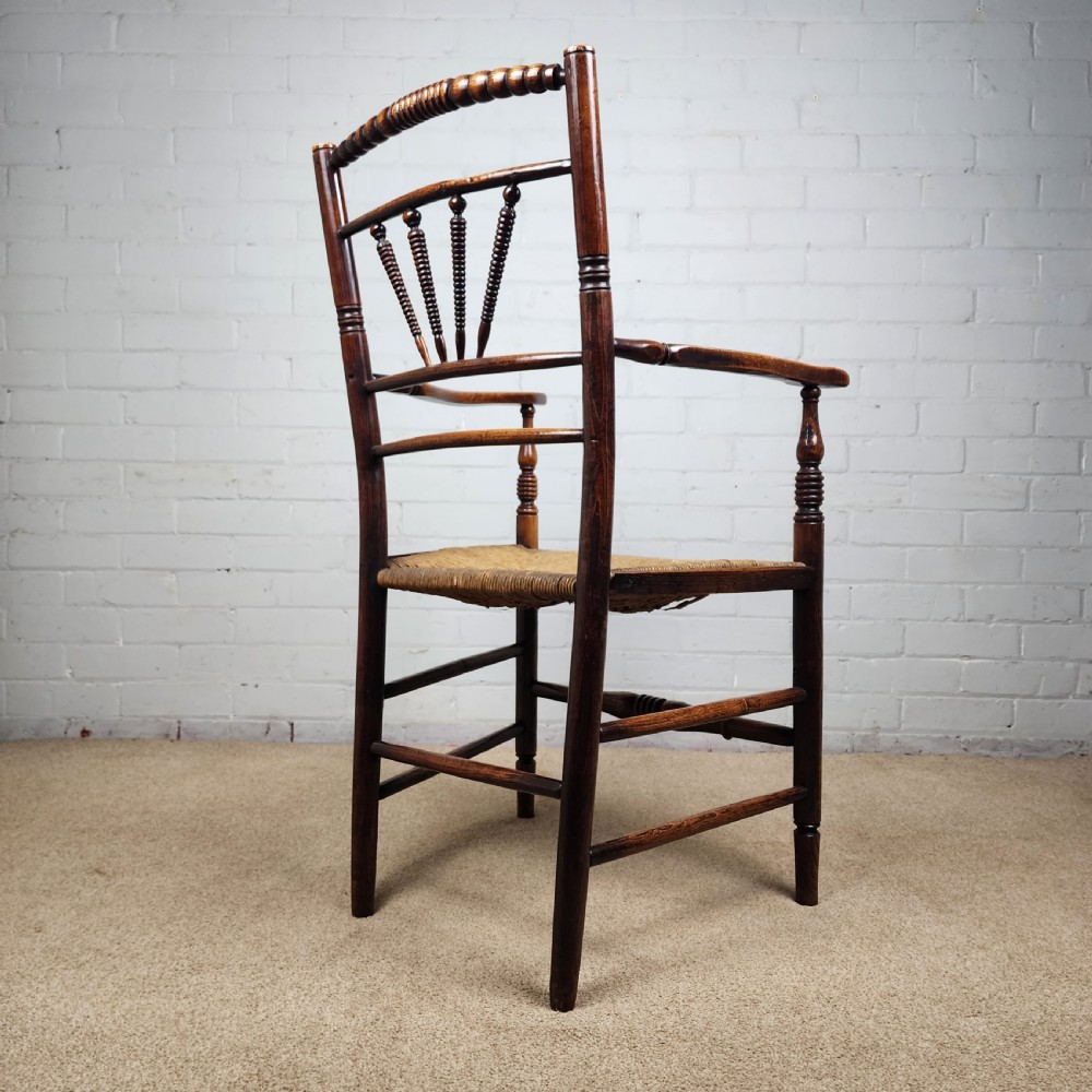 A George III elm and fruitwood carver chair featuring turned back spindles, shaped armrests, and a woven rush seat. View IX