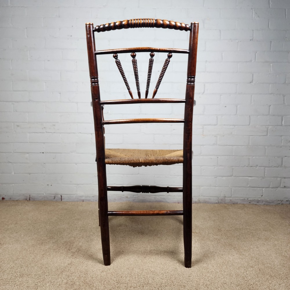 A George III elm and fruitwood carver chair featuring turned back spindles, shaped armrests, and a woven rush seat. View X