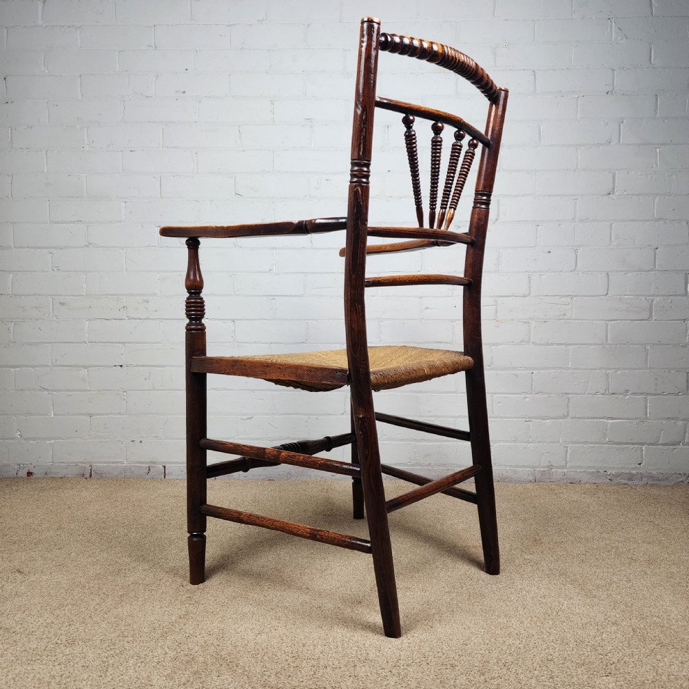 A George III elm and fruitwood carver chair featuring turned back spindles, shaped armrests, and a woven rush seat. View XI