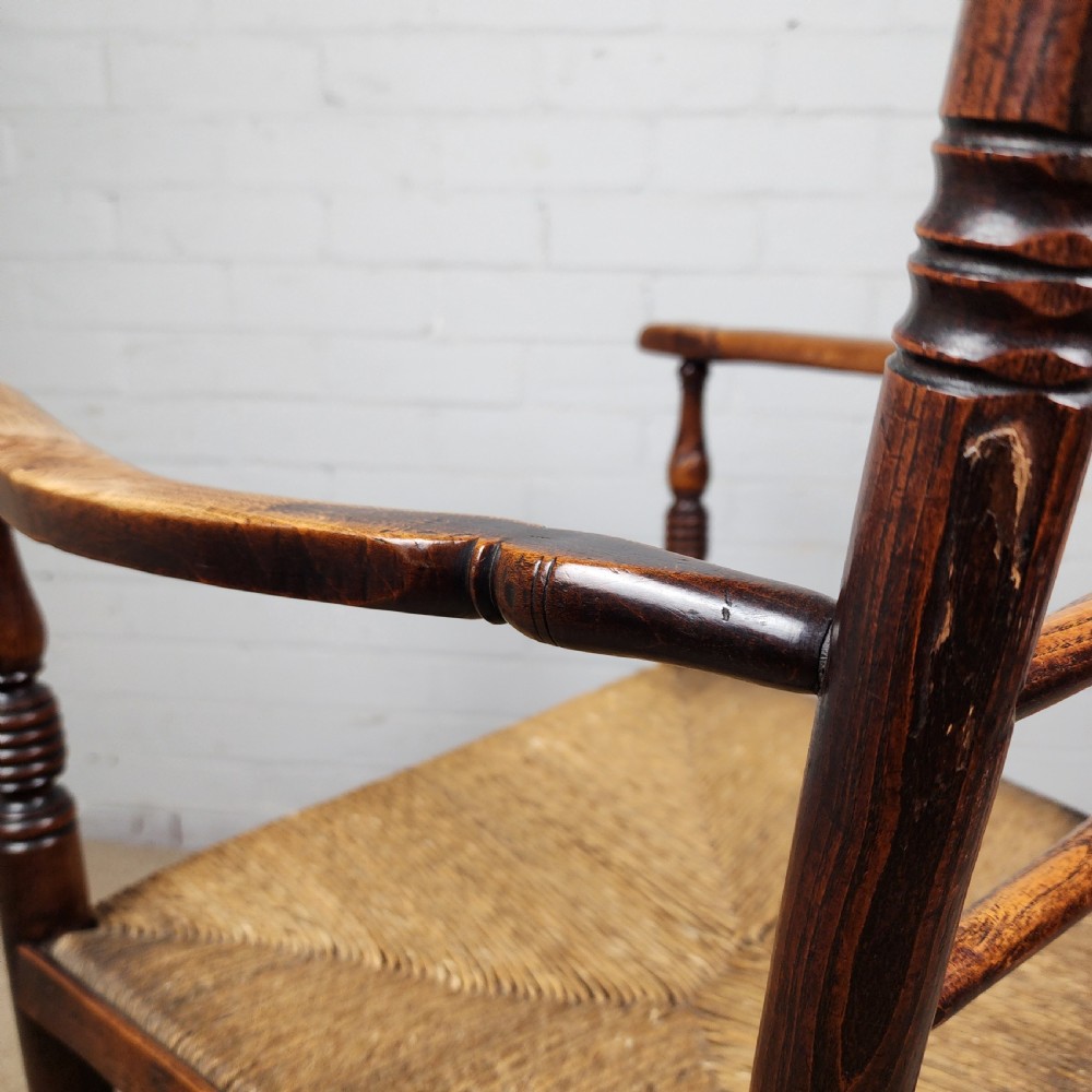 A George III elm and fruitwood carver chair featuring turned back spindles, shaped armrests, and a woven rush seat. View XII