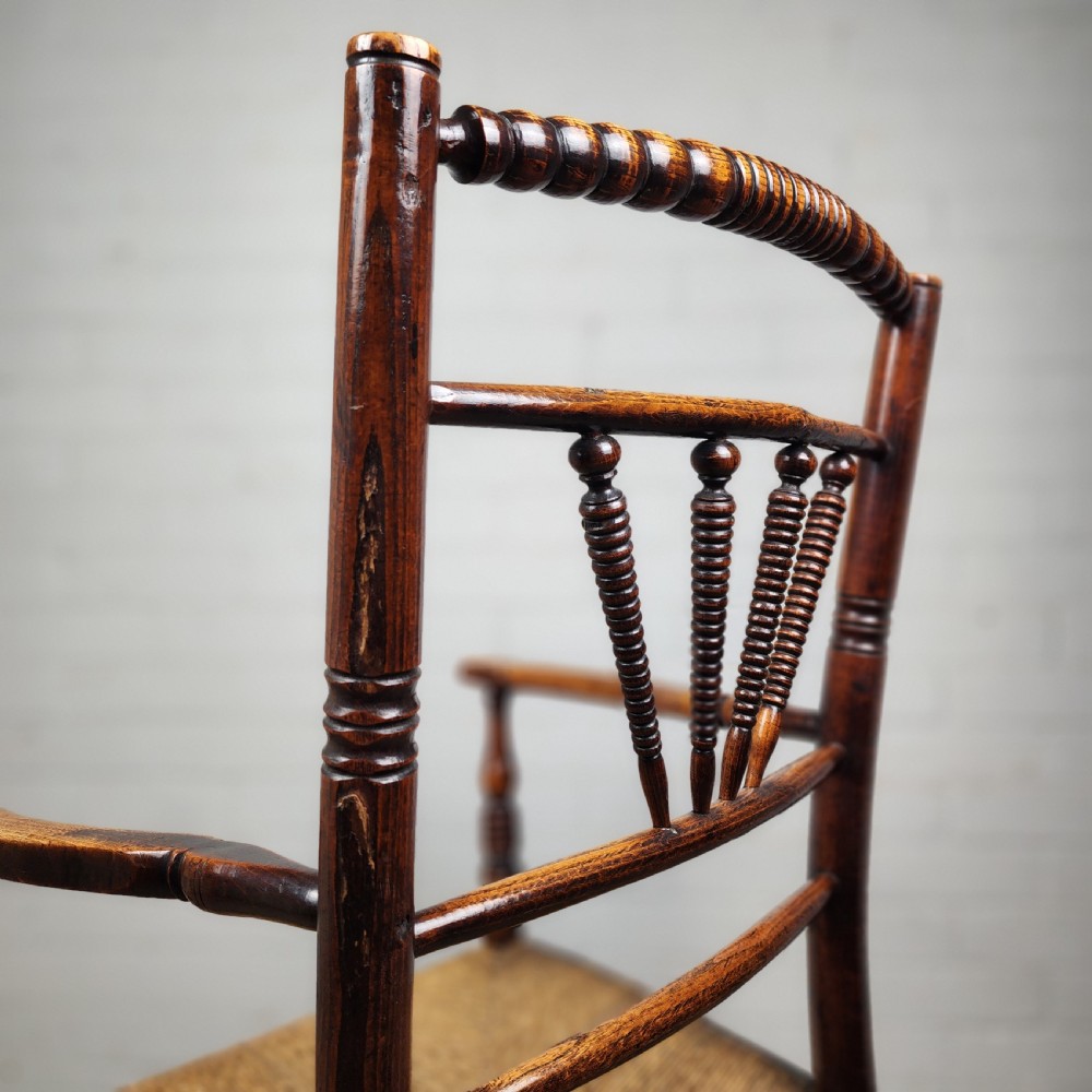 A George III elm and fruitwood carver chair featuring turned back spindles, shaped armrests, and a woven rush seat. View XIII