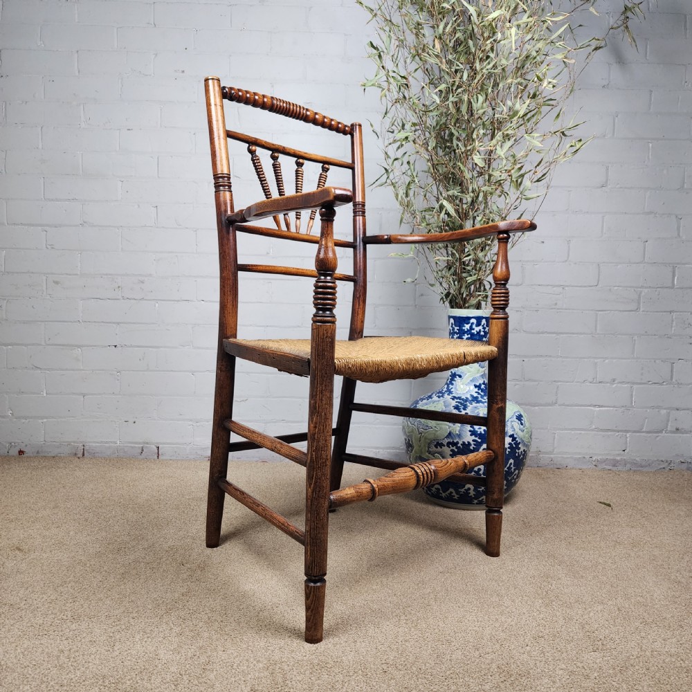 A George III elm and fruitwood carver chair featuring turned back spindles, shaped armrests, and a woven rush seat.
