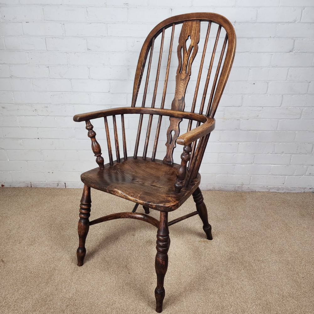 A 19th-century dark wood Windsor armchair featuring a high hoop back, pierced splat, turned legs, and a shaped elm seat.
