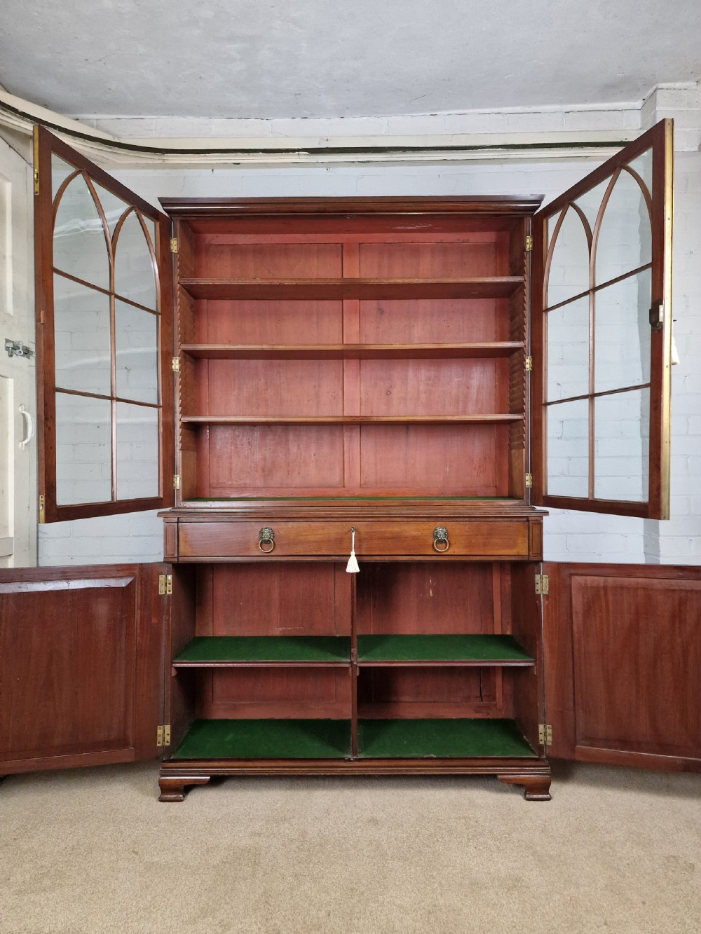 A George IV mahogany bookcase cupboard featuring glazed upper doors with Gothic arch glazing bars above a lower panelled cupboard. View II