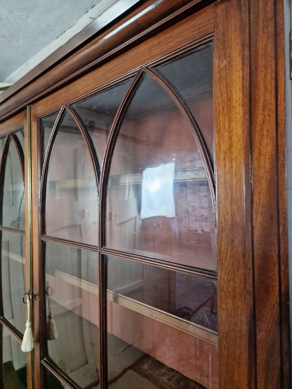 A George IV mahogany bookcase cupboard featuring glazed upper doors with Gothic arch glazing bars above a lower panelled cupboard. View VI