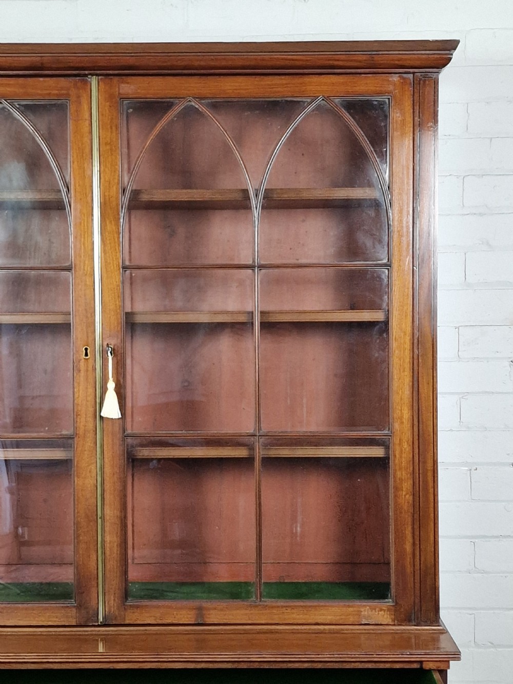 A George IV mahogany bookcase cupboard featuring glazed upper doors with Gothic arch glazing bars above a lower panelled cupboard. View VII
