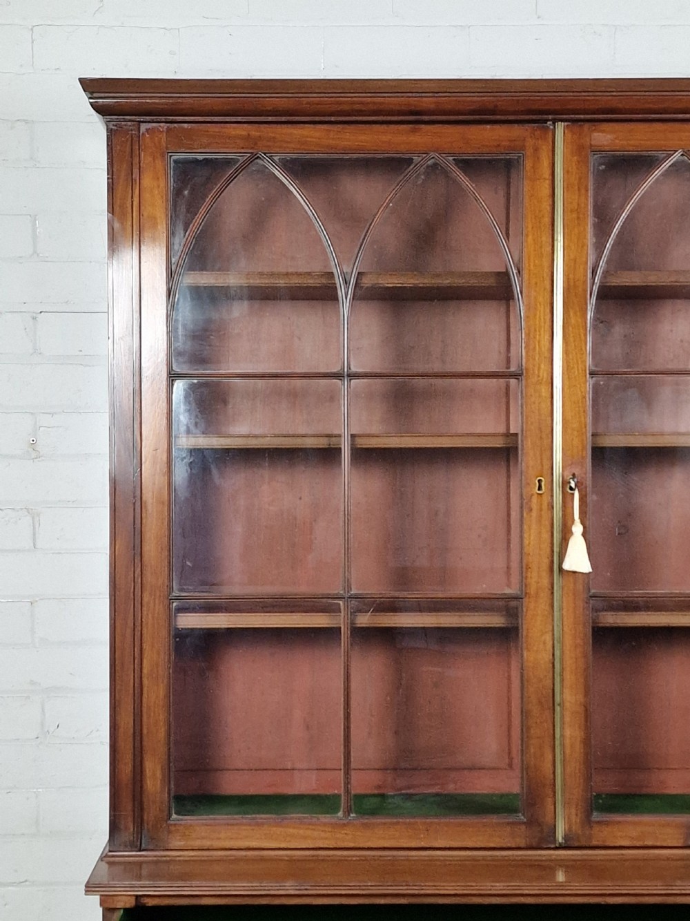 A George IV mahogany bookcase cupboard featuring glazed upper doors with Gothic arch glazing bars above a lower panelled cupboard. View VIII