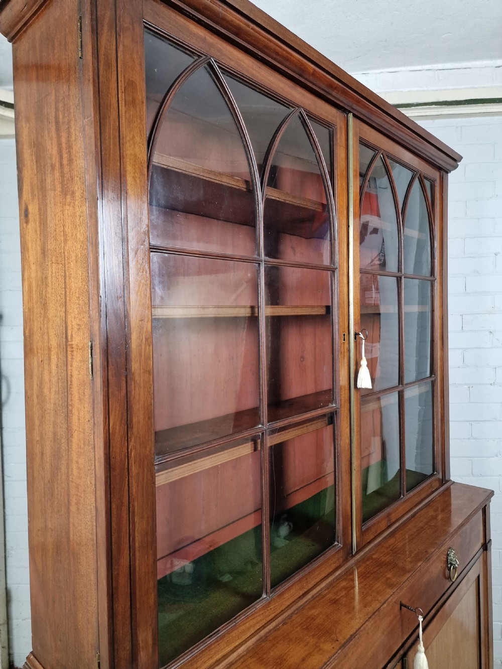 A George IV mahogany bookcase cupboard featuring glazed upper doors with Gothic arch glazing bars above a lower panelled cupboard. View XVII
