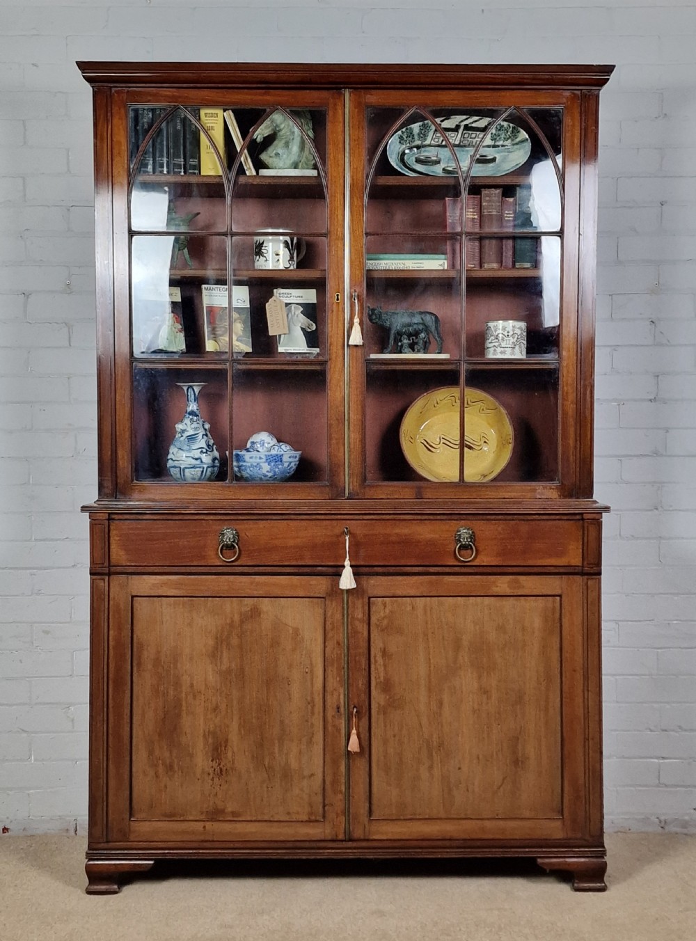 A George IV mahogany bookcase cupboard featuring glazed upper doors with Gothic arch glazing bars above a lower panelled cupboard. View XIX