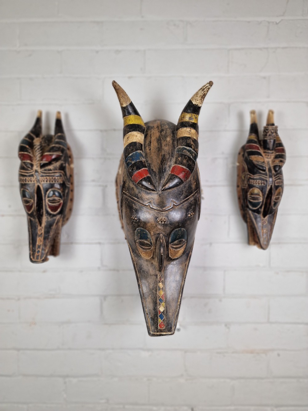 A carved wooden Guro Zamble helmet mask featuring an open-jawed snout with carved white teeth, red painted interior, dark horns, and woven fibre stitching along the base. View XII