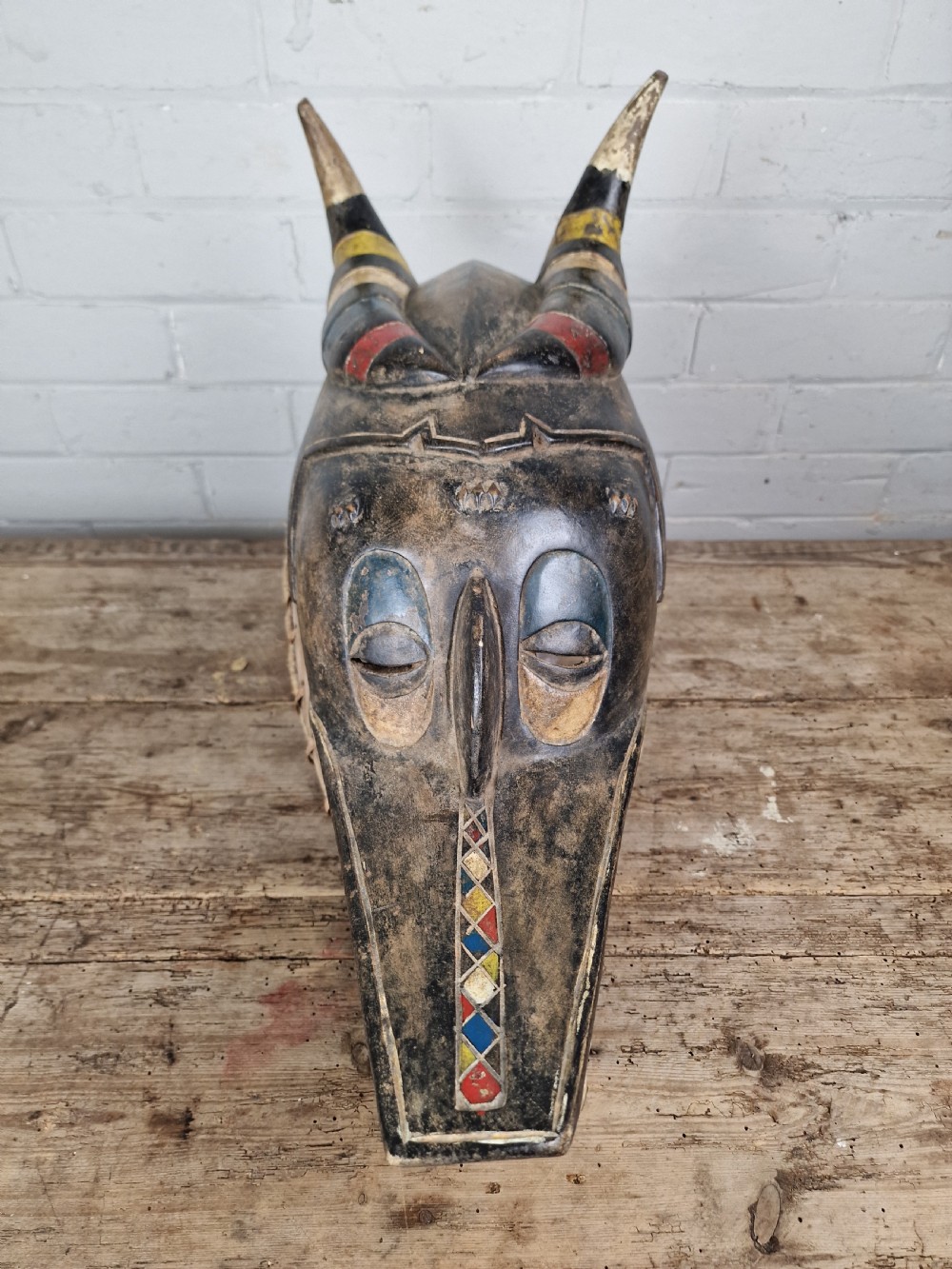 A carved wooden Guro Zamble helmet mask featuring an open-jawed snout with carved white teeth, red painted interior, dark horns, and woven fibre stitching along the base. View XI