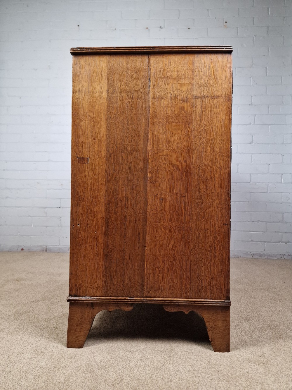 An antique Georgian oak chest of drawers featuring a two-over-three drawer configuration with oval brass drop handles and bracket feet. View II