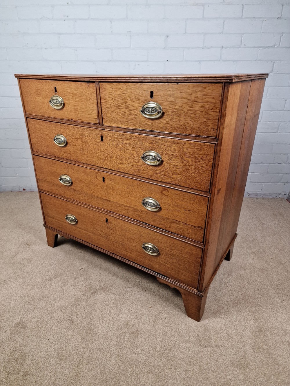 An antique Georgian oak chest of drawers featuring a two-over-three drawer configuration with oval brass drop handles and bracket feet. View III