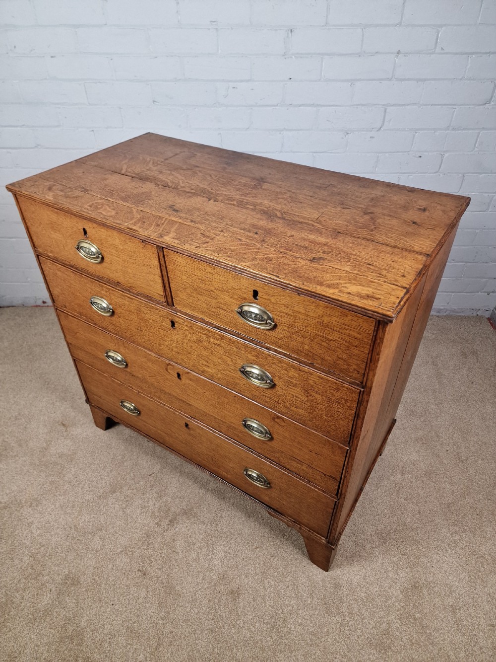 An antique Georgian oak chest of drawers featuring a two-over-three drawer configuration with oval brass drop handles and bracket feet. View IV