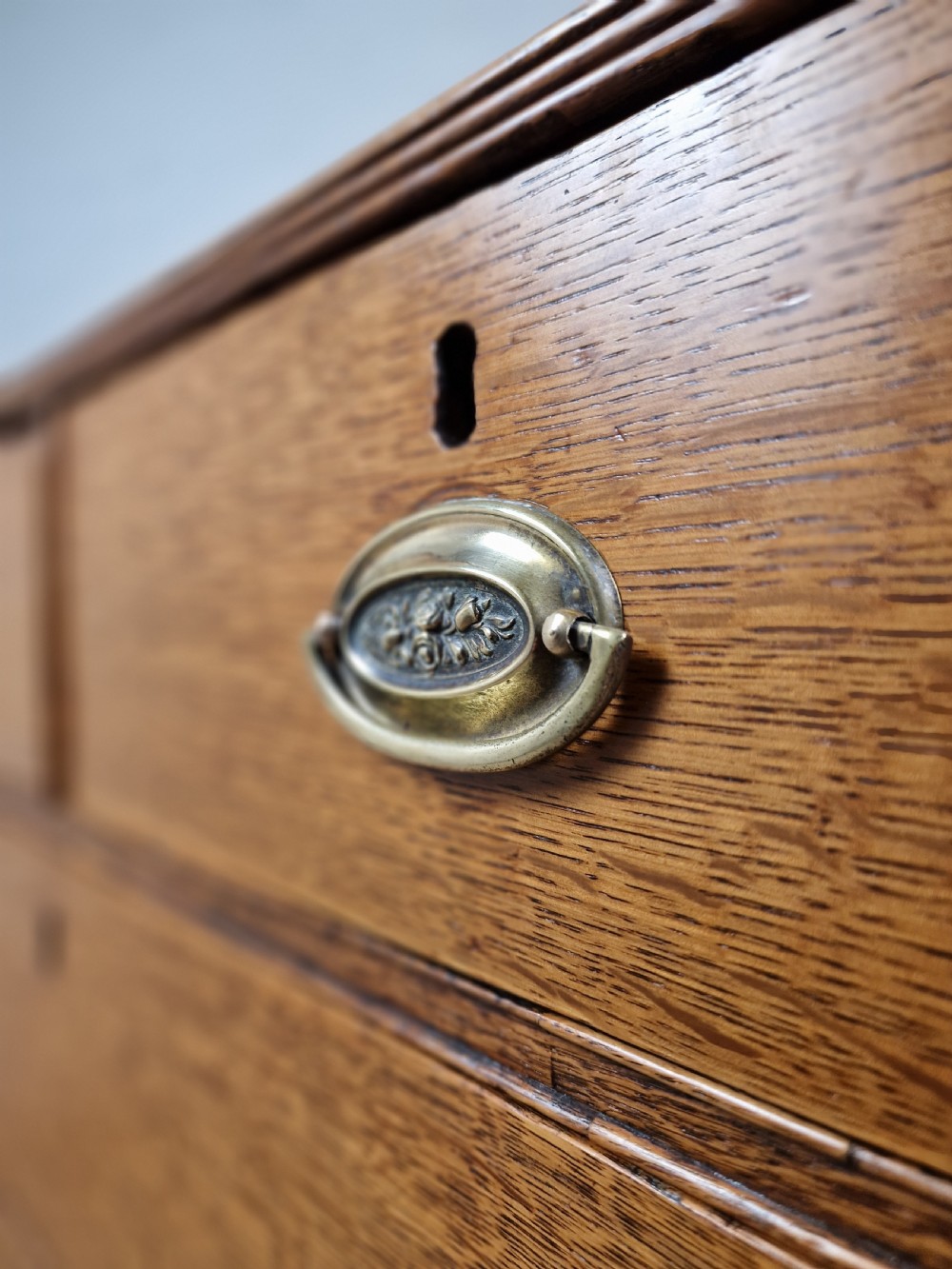 An antique Georgian oak chest of drawers featuring a two-over-three drawer configuration with oval brass drop handles and bracket feet. View V