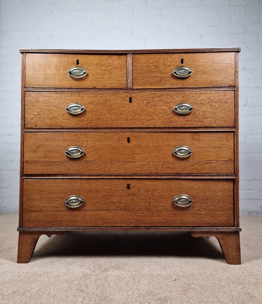 An antique Georgian oak chest of drawers featuring a two-over-three drawer configuration with oval brass drop handles and bracket feet.