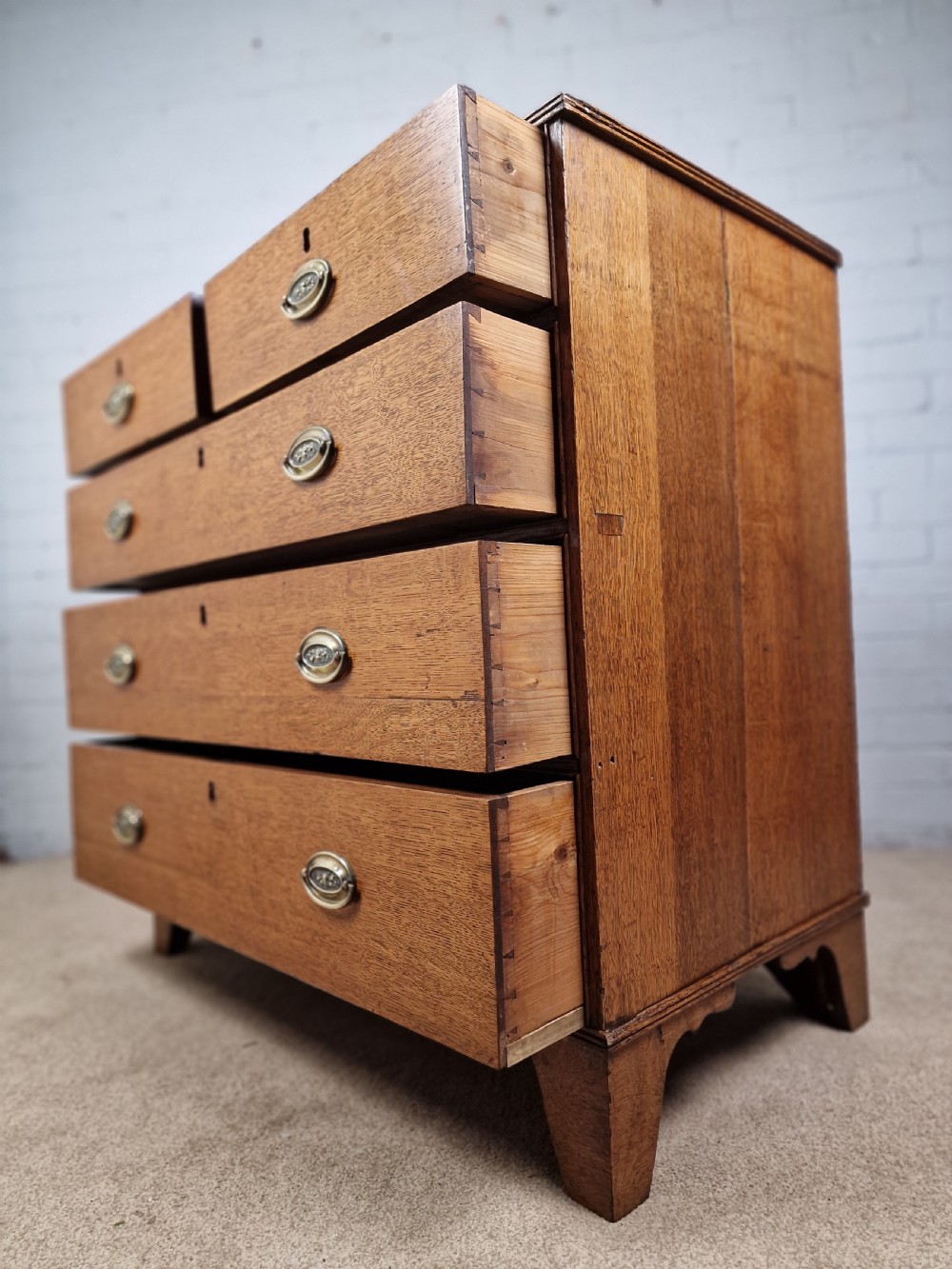 An antique Georgian oak chest of drawers featuring a two-over-three drawer configuration with oval brass drop handles and bracket feet. View VII