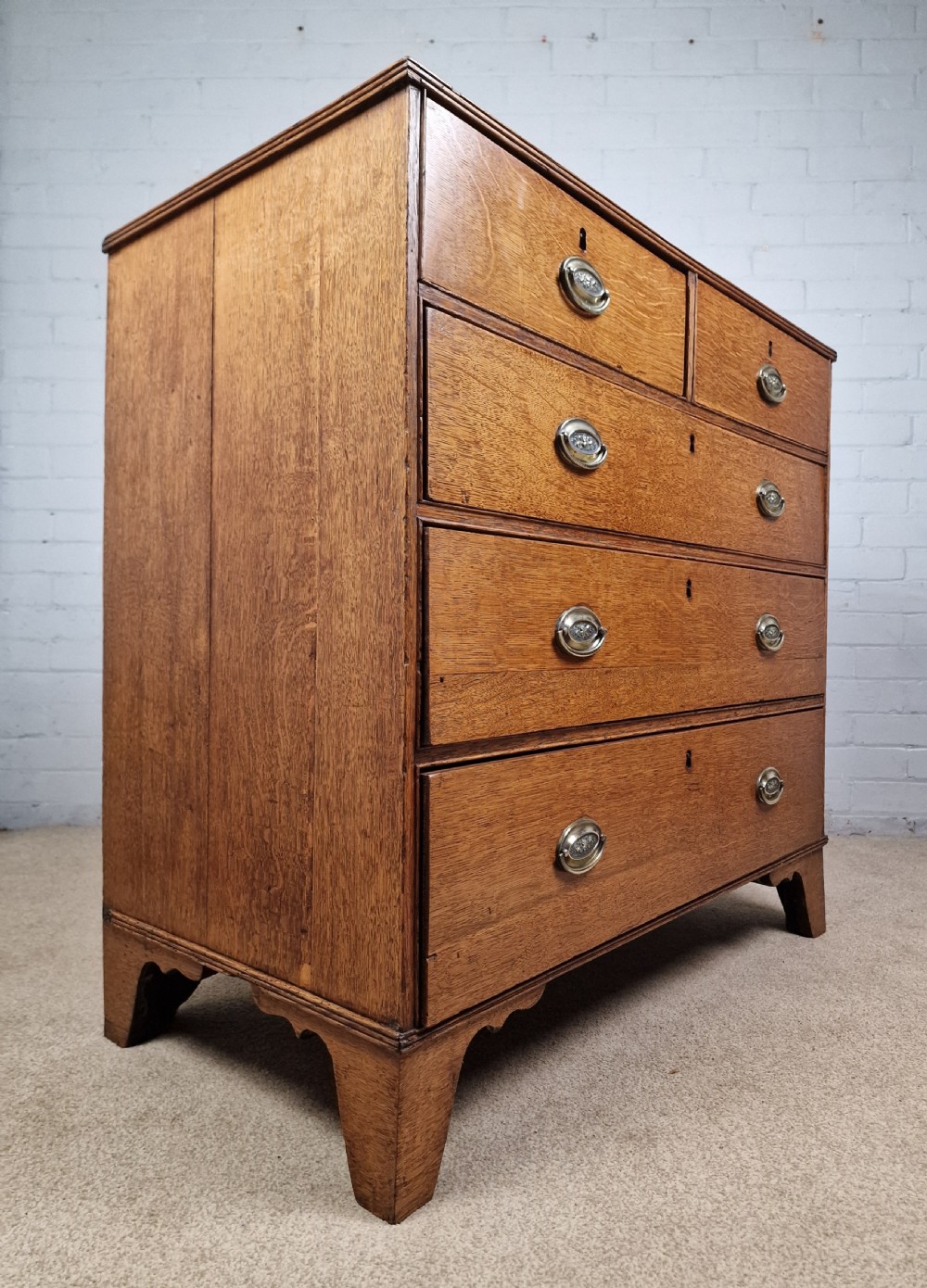 An antique Georgian oak chest of drawers featuring a two-over-three drawer configuration with oval brass drop handles and bracket feet. View IX