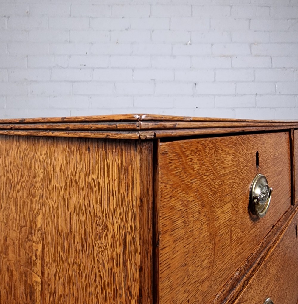 An antique Georgian oak chest of drawers featuring a two-over-three drawer configuration with oval brass drop handles and bracket feet. View X