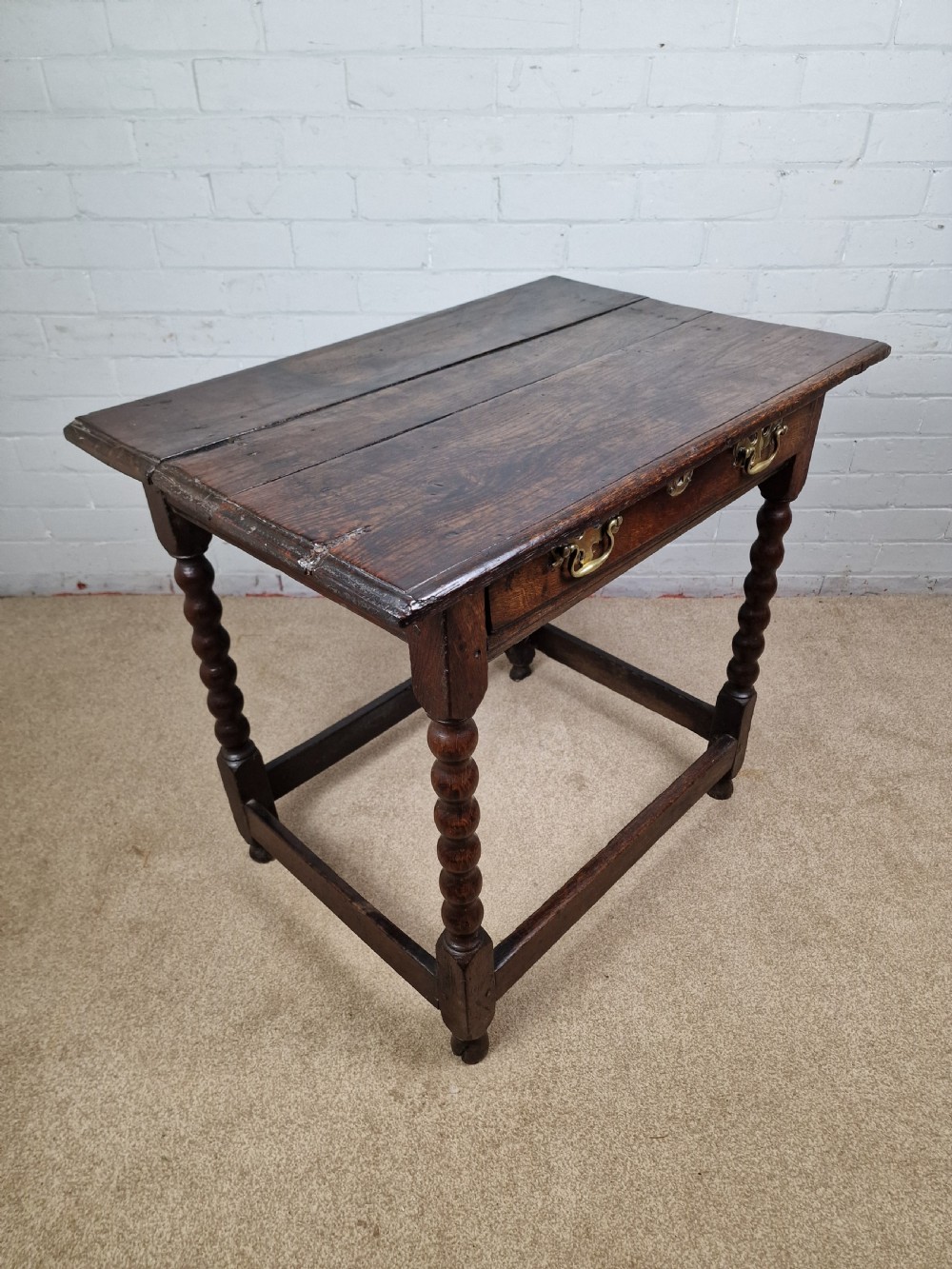 An 18th-century dark oak side table featuring four bobbin-turned legs, a square top, a single drawer with brass handles, and a box stretcher. View II