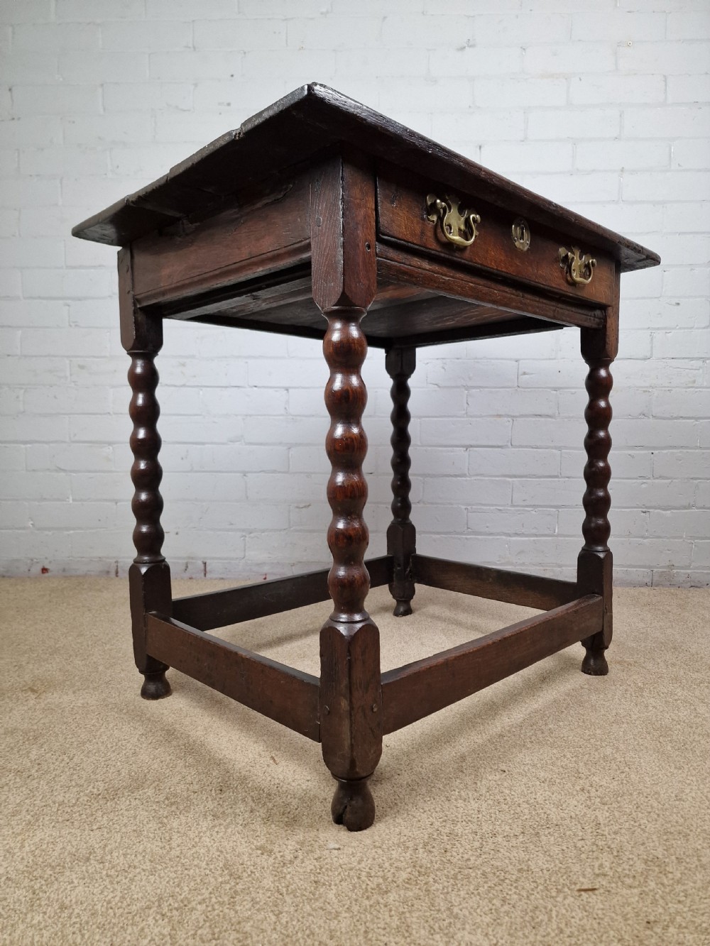 An 18th-century dark oak side table featuring four bobbin-turned legs, a square top, a single drawer with brass handles, and a box stretcher. View III
