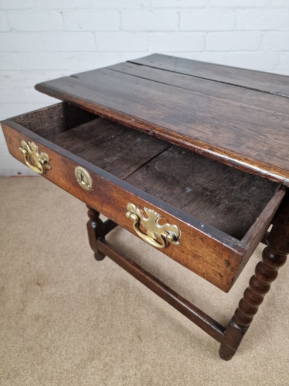 An 18th-century dark oak side table featuring four bobbin-turned legs, a square top, a single drawer with brass handles, and a box stretcher. View IV