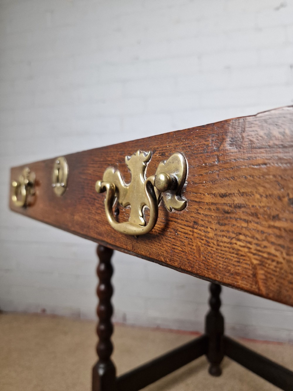 An 18th-century dark oak side table featuring four bobbin-turned legs, a square top, a single drawer with brass handles, and a box stretcher. View V