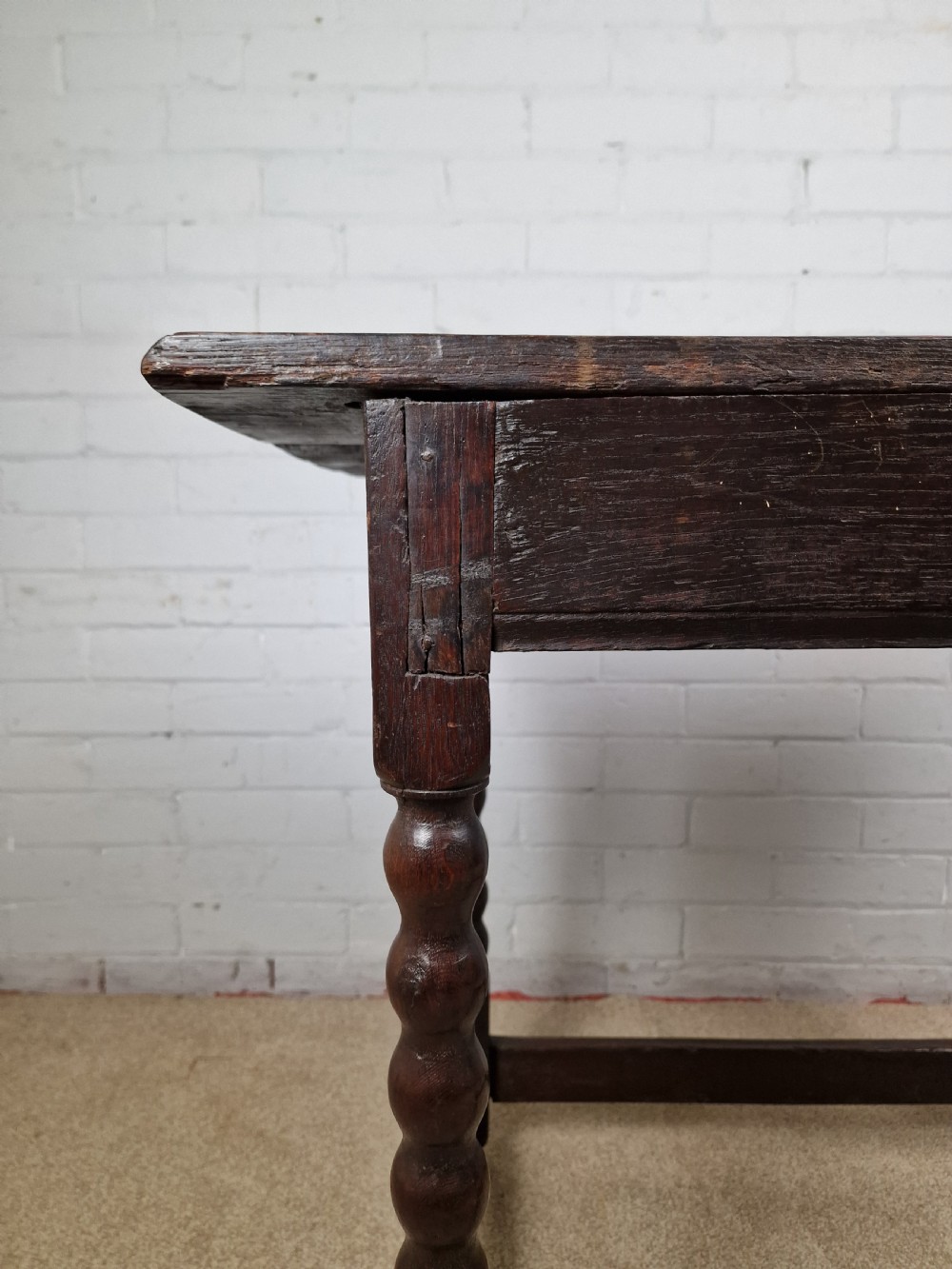 An 18th-century dark oak side table featuring four bobbin-turned legs, a square top, a single drawer with brass handles, and a box stretcher. View VII
