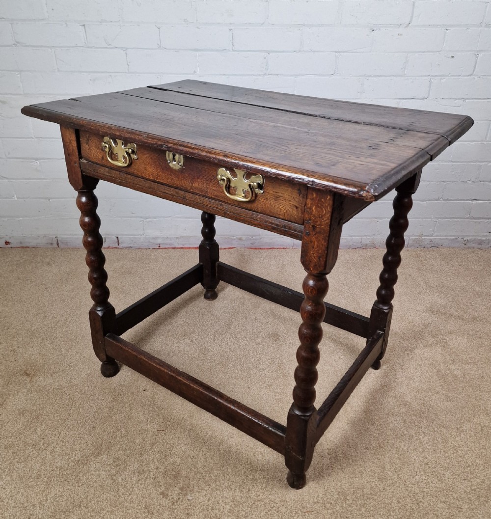 An 18th-century dark oak side table featuring four bobbin-turned legs, a square top, a single drawer with brass handles, and a box stretcher. View IX
