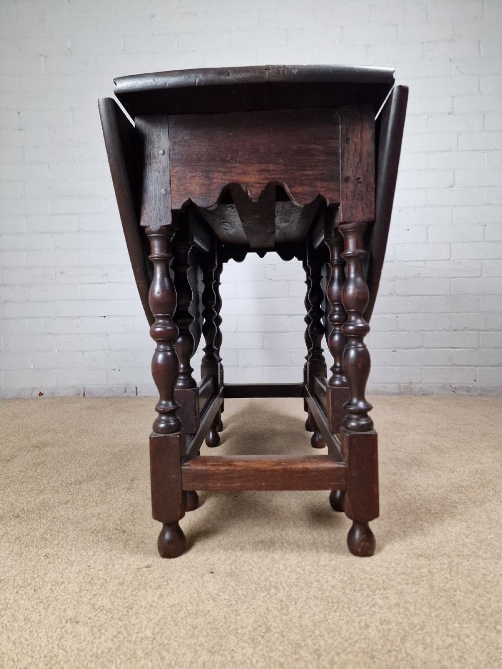 An 18th-century dark oak gateleg table featuring folded drop leaves, turned legs, and lower stretchers. View II