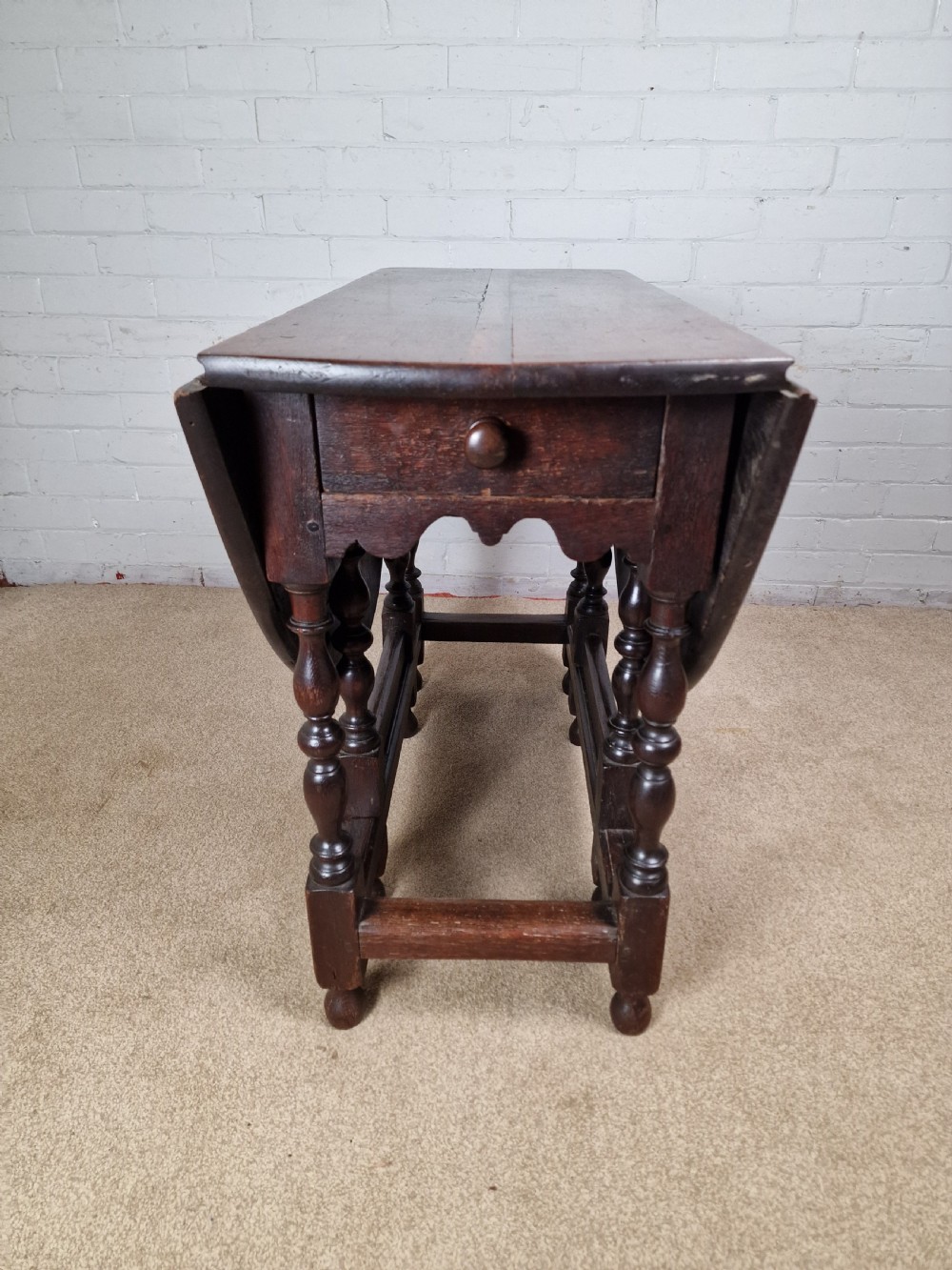 An 18th-century dark oak gateleg table featuring folded drop leaves, turned legs, and lower stretchers. View III