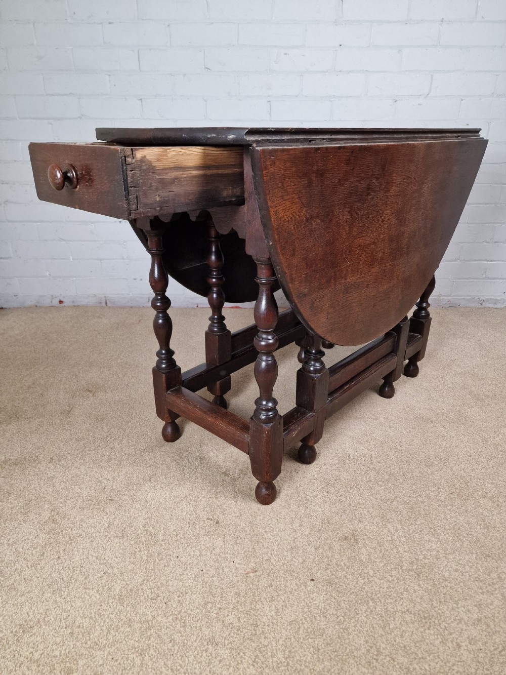 An 18th-century dark oak gateleg table featuring folded drop leaves, turned legs, and lower stretchers. View V