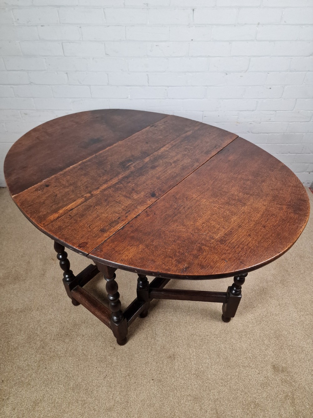 An 18th-century dark oak gateleg table featuring folded drop leaves, turned legs, and lower stretchers. View VI