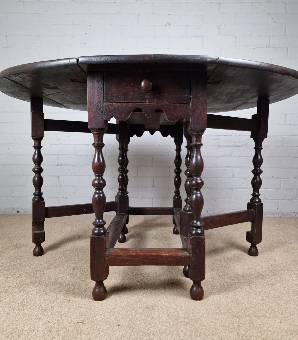 An 18th-century dark oak gateleg table featuring folded drop leaves, turned legs, and lower stretchers. View IX