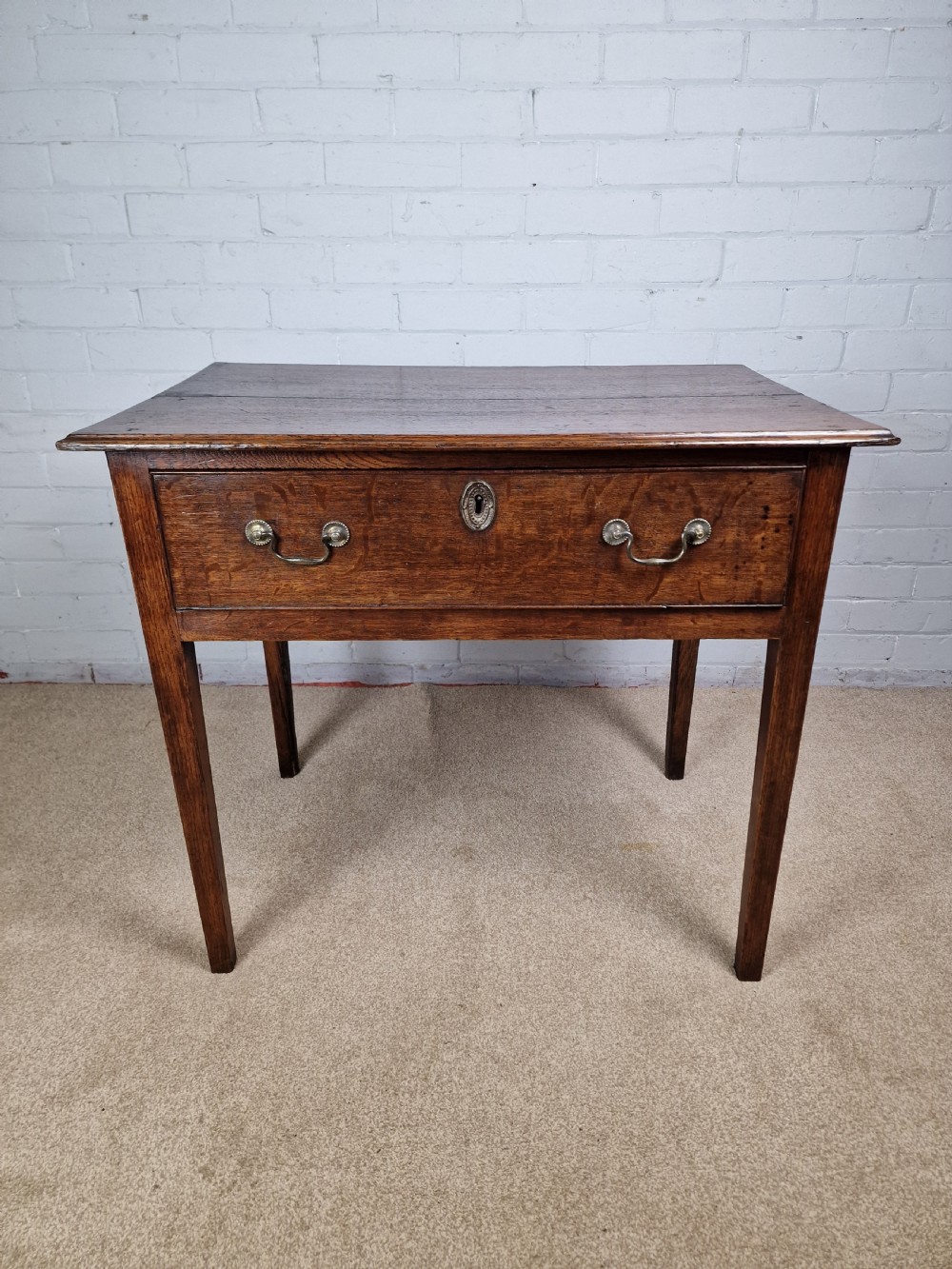 An 18th-century antique oak lowboy side table featuring a single wide drawer with brass handles and square tapered legs. View XIV