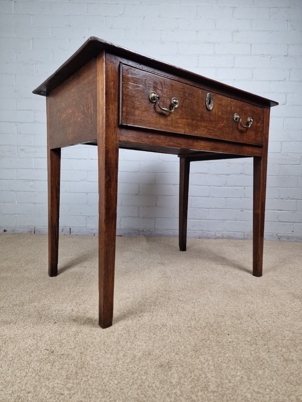 An 18th-century antique oak lowboy side table featuring a single wide drawer with brass handles and square tapered legs. View II