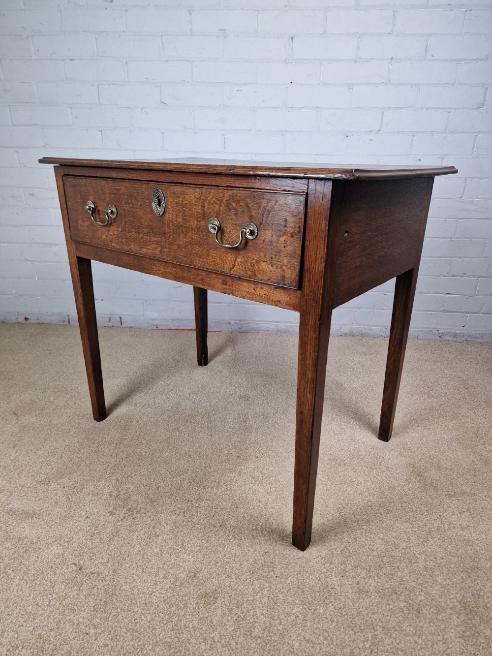 An 18th-century antique oak lowboy side table featuring a single wide drawer with brass handles and square tapered legs. View III