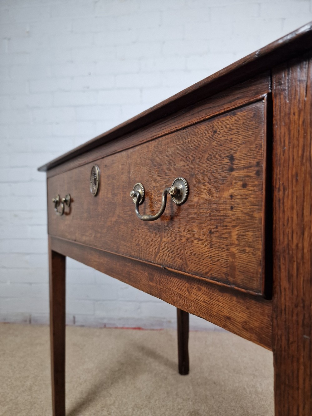 An 18th-century antique oak lowboy side table featuring a single wide drawer with brass handles and square tapered legs. View V