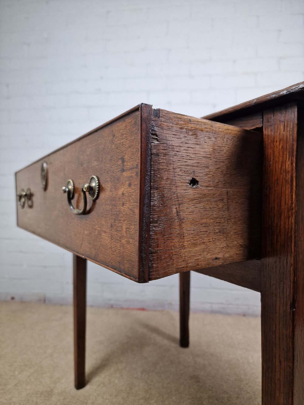 An 18th-century antique oak lowboy side table featuring a single wide drawer with brass handles and square tapered legs. View VI