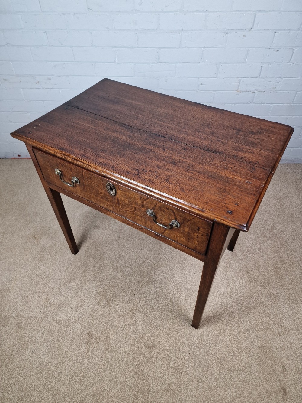 An 18th-century antique oak lowboy side table featuring a single wide drawer with brass handles and square tapered legs. View XI