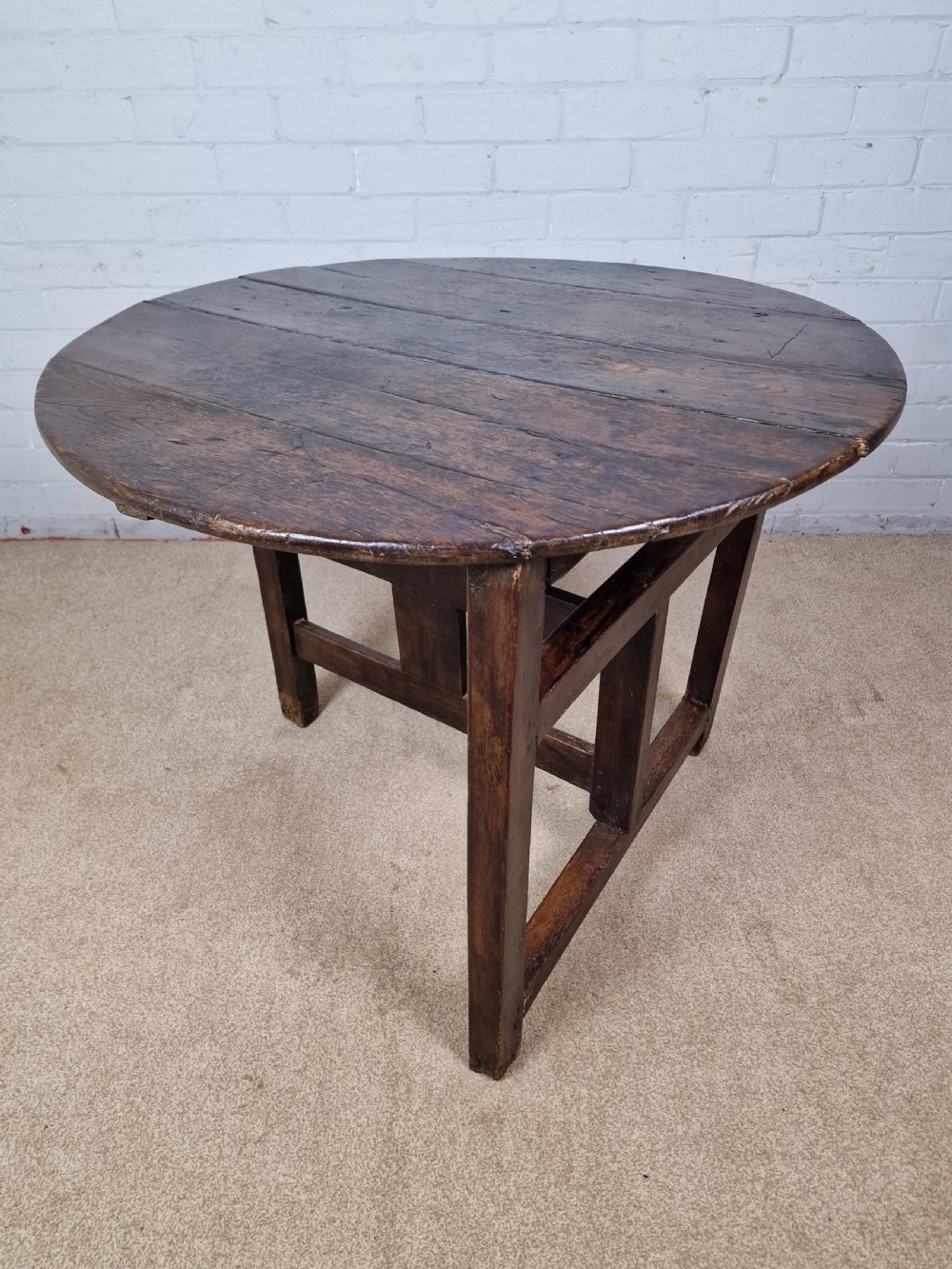 A circular dark oak George III coaching table featuring a planked top and a folding wooden base structure.