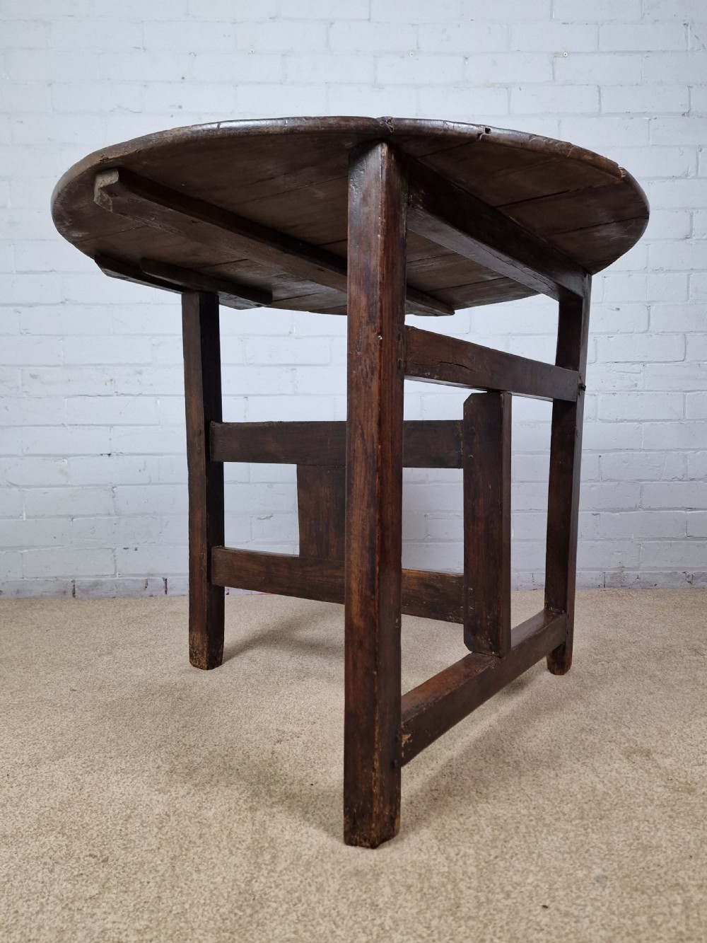 A circular dark oak George III coaching table featuring a planked top and a folding wooden base structure. View II